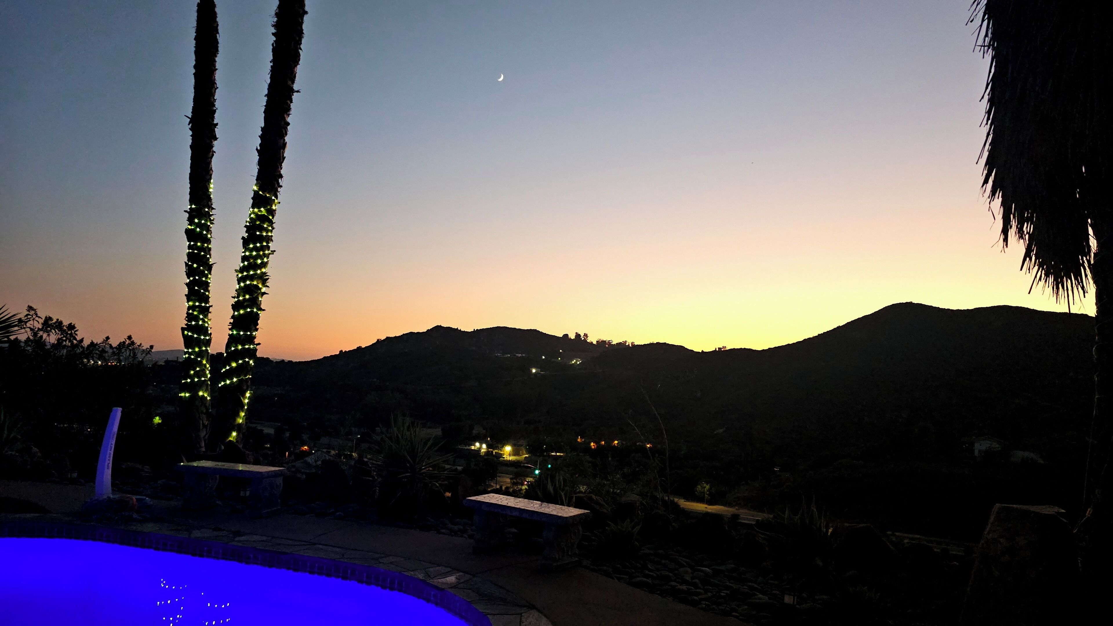 A pool area with a view of mountains and a crescent moon in the sky.