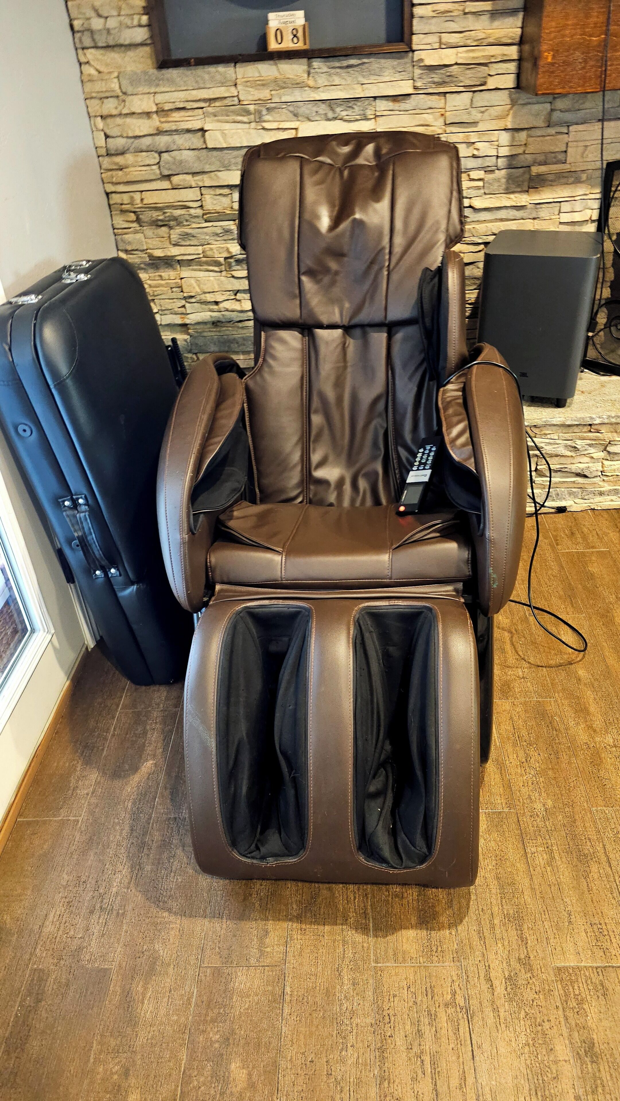 A massage chair in a room with a stone wall and a television above it.