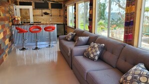 Un intérieur chaleureux avec un plafond en bois, un canapé agrémenté de coussins à motifs et un coin bar avec des tabourets rouges.