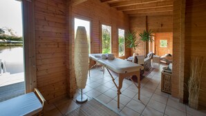 Een houten hut met een massagetafel, een stoel en een potplant.