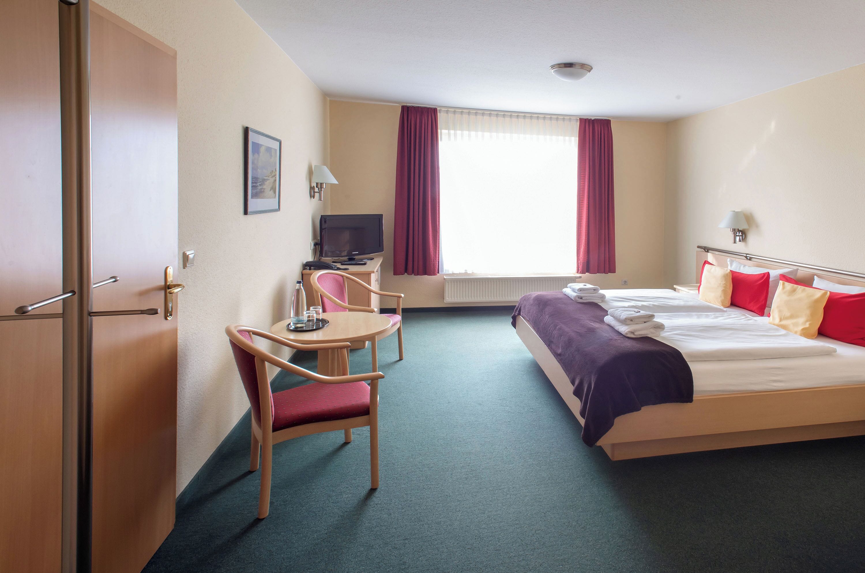 A hotel room with a bed, a desk with a chair, a television, and a window with curtains.