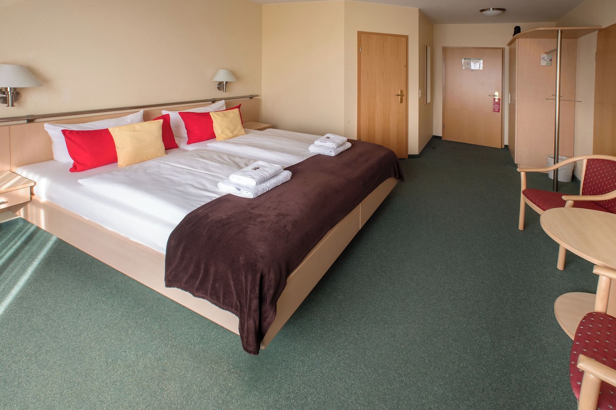 A hotel room with a large bed, a desk, and a chair.