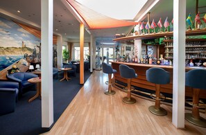 A bar area with wooden flooring, blue bar stools, and a mural of a seascape on the wall. - Hotel & Restaurant Zum Kap Arkona (Putgarten)