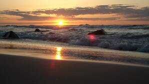 Een strand bij zonsondergang met golven en rotsen.