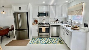 A modern kitchen with white cabinets, stainless steel appliances, a microwave, a stove, and a sink. - Exquisite Waterfront Villa (Jolly Harbour)