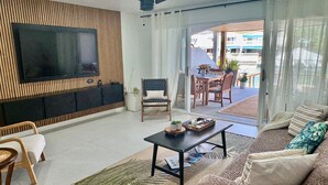 A modern living room with a flat-screen TV, a ceiling fan, a sofa, a coffee table, and a dining area with a table and chairs. - Exquisite Waterfront Villa (Jolly Harbour)