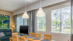 Un salón moderno con sofá, televisor, mesa de comedor con sillas y ventanas grandes con persianas.