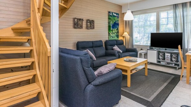 Una sala de estar moderna con una escalera de madera, un conjunto de sofás, una mesa de centro, un televisor y un sistema de sonido montado en la pared.