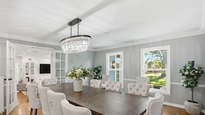 A spacious dining room with a large wooden table, white upholstered chairs, and a crystal chandelier. - Luxury Lakeview Home w/ Pool | Perfect for Events (dade city)