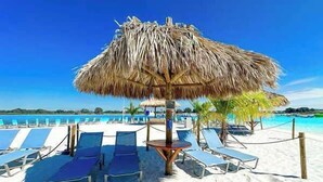 A beach with thatched umbrellas, lounge chairs, and a clear blue sky. - Luxury Lakeview Home w/ Pool | Perfect for Events (dade city)