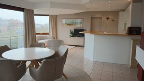 Una sala de estar moderna con comedor, cocina y un balcón con vistas a edificios.