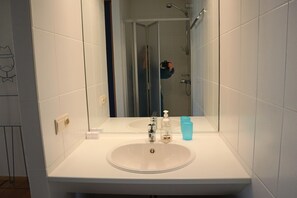 Une salle de bain avec un lavabo blanc, un miroir et une douche.