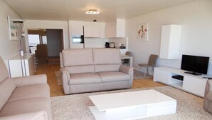 Una sala de estar moderna con un sofá color beige, una mesa de centro blanca y un televisor sobre un mueble blanco.