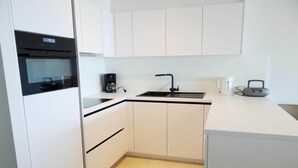 Una cocina moderna con armarios blancos, un horno negro, una cafetera y una radio.