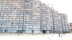 Un edificio de varios pisos con fachada uniforme, balcones y una estructura central de vidrio.