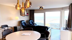 A hotel room with a large window, a round table, two black leather chairs, a desk with a computer, and a lamp. - Apartment in Nieuwpoort near the Beach (Nieuwpoort)