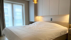 A bedroom with a large bed, a sliding glass door, and a wall-mounted light fixture. - Apartment in Nieuwpoort near the Beach (Nieuwpoort)