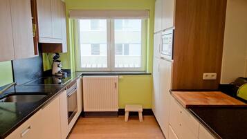 A compact kitchen with a window, a radiator, and wooden cabinets.