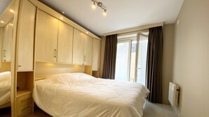 A hotel room with a large bed, built-in wardrobe, and a window with curtains. - Apartment in Nieuwpoort near the Beach (Nieuwpoort)