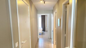 A hallway with white doors, a light fixture, and a bed in the distance. - Apartment in Nieuwpoort near the Beach (Nieuwpoort)
