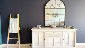 A room with a dark blue wall, a white cabinet with drawers, a wooden ladder, and a large mirror with a clock. - Apartment in Nieuwpoort with Sea Views (Nieuwpoort)