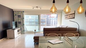 A modern living room with a glass table, a sofa, and a TV on a wooden cabinet. - Apartment in Nieuwpoort with Sea Views (Nieuwpoort)