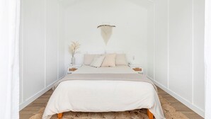 A minimalist bedroom with a bed centered in the room, flanked by nightstands and a hanging macrame light fixture. - Long Island Beach Getaway (Frankston)