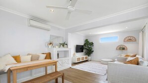 A modern living room with a white sofa, a wooden bench, a TV, and a ceiling fan. - Long Island Beach Getaway (Frankston)