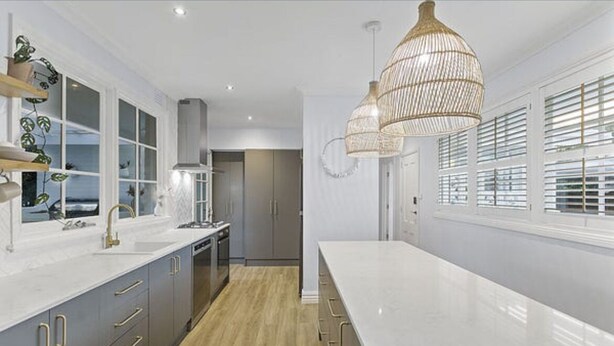A modern kitchen with a long countertop, grey cabinets, and a large window with blinds. - Long Island Beach Getaway (Frankston)