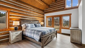 Une chambre située dans une cabane en rondins, avec un lit, des tables de chevet et de grandes fenêtres.