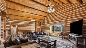 L'intérieur d'une cabane en rondins, avec un plafond en bois, un grand téléviseur et un coin salon confortable comprenant un canapé et des fauteuils.