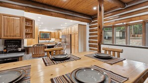 L’intérieur d’un chalet rustique, avec des poutres en bois, un coin repas avec une table dressée pour quatre personnes et une cuisine dotée de meubles en bois.