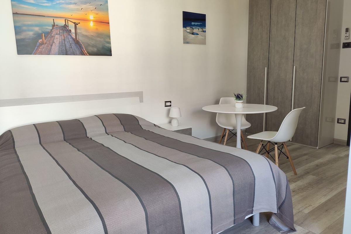 A bedroom with a bed, a small round table, two chairs, a nightstand, and a wardrobe.