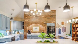 Una cocina con un arco de ladrillo, luces colgantes modernas y una isla central con una bandeja de manzanas verdes.
