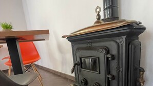 A black wood-burning stove with a chimney, a red chair, and a small plant on a table. - CASALE CONTI (Castellabate)