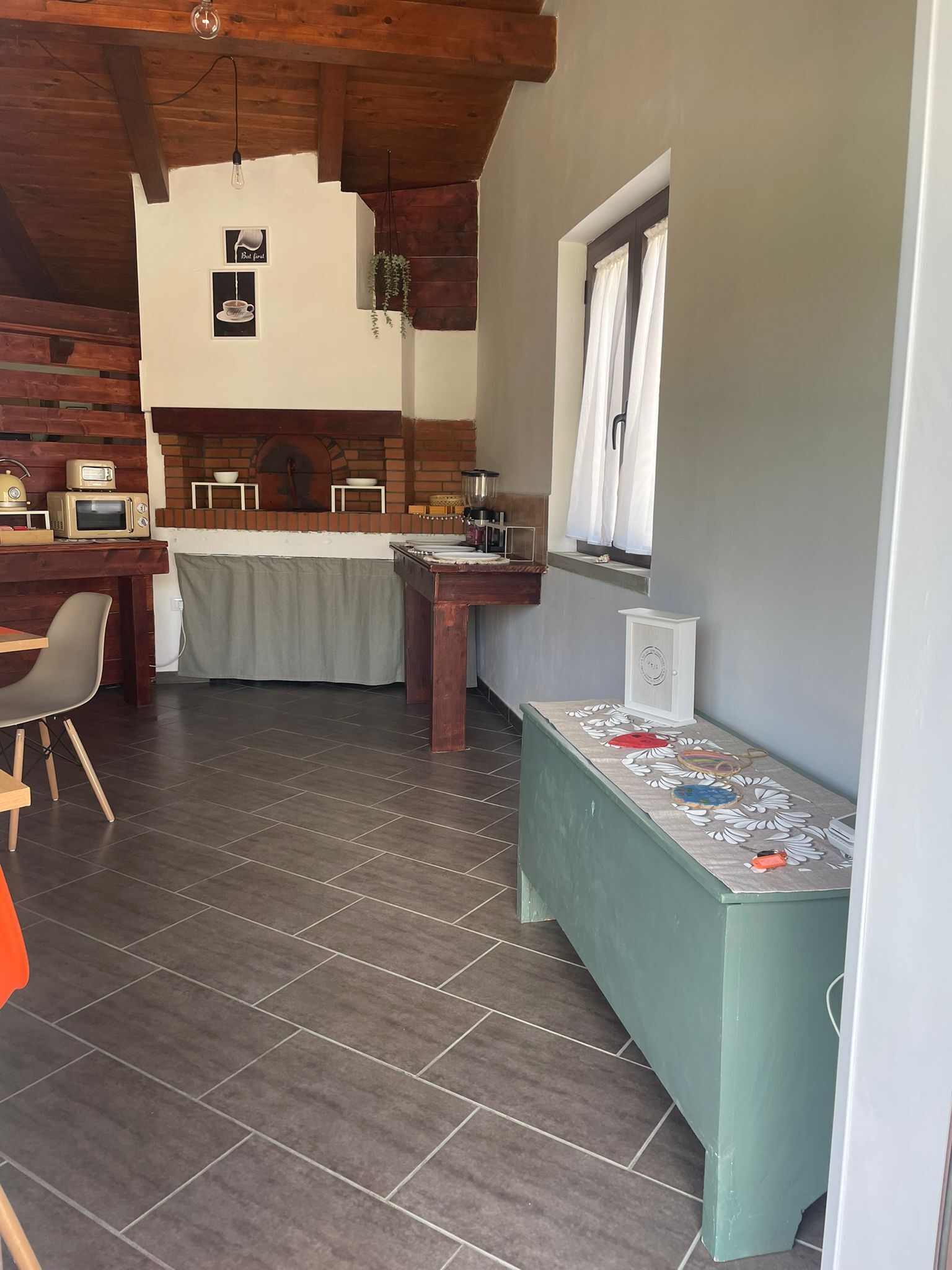 A kitchen with a brick oven, a dining area with a table and chairs, and a window with curtains.