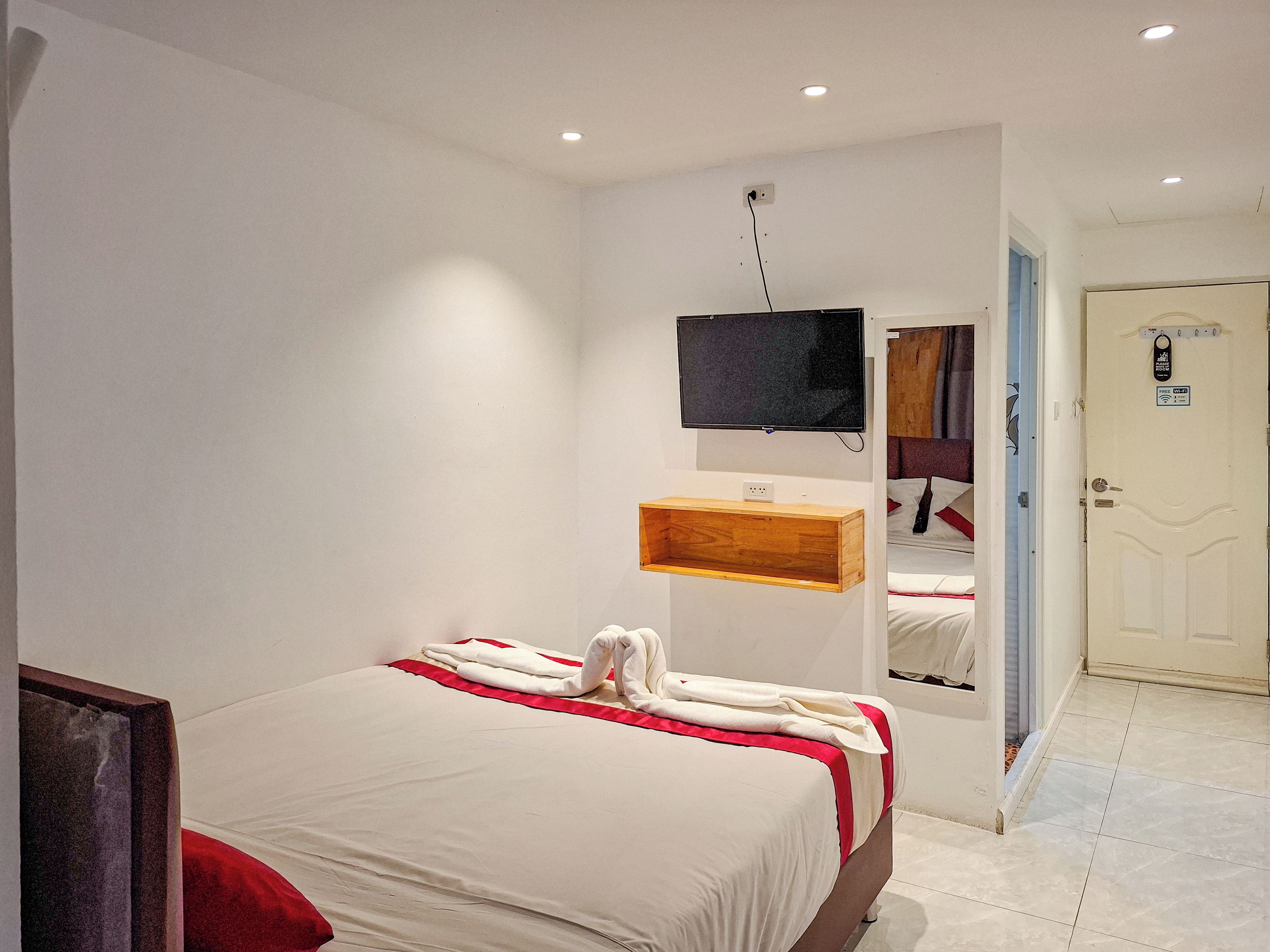 Ein Hotelzimmer mit einem Bett, einem an der Wand befestigten Fernseher, einem hölzernen Regal und einer Tür mit einem Schild.