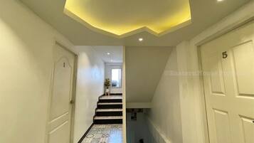 A hallway with a staircase, white walls, and a ceiling with recessed lighting.