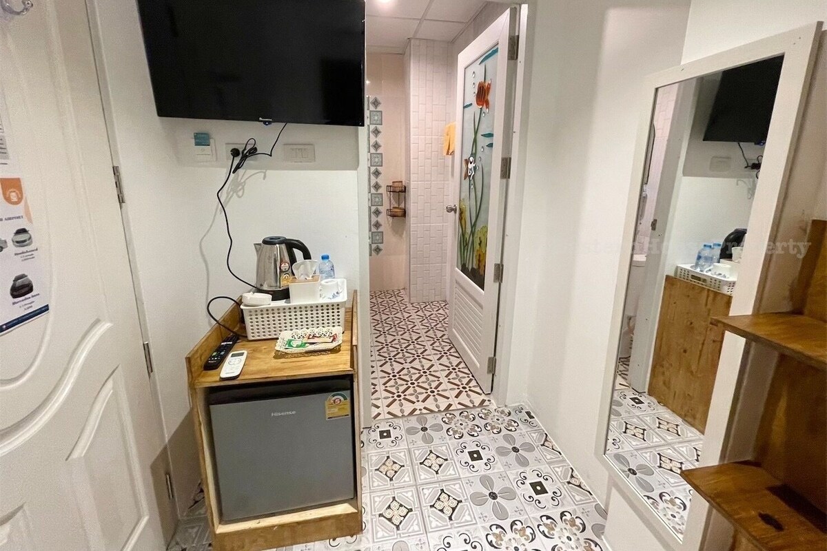 En smal hall med ett kaklat golv, ett litet kylskåp, ett handfat och en spegel.