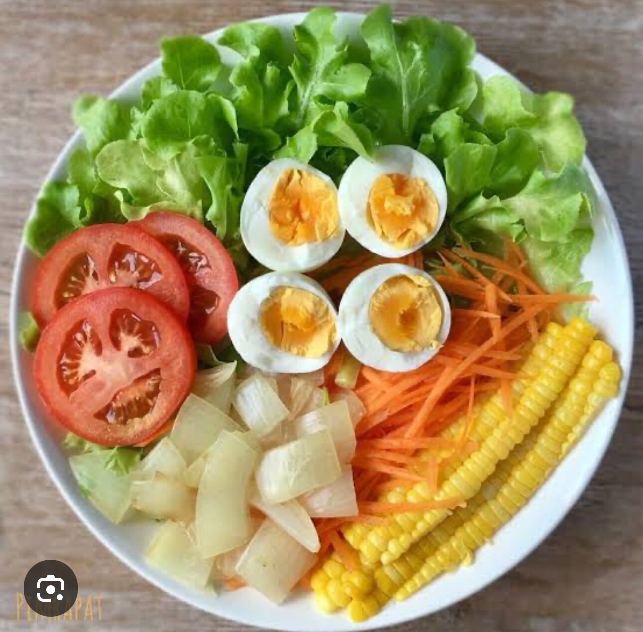 Eine Salatschüssel mit Blattsalat, Tomaten, gekochten Eiern, geriebenen Karotten, Mais und gewürfelten Kartoffeln.