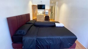 Habitació d'hotel moderna amb un llit gran, un armari de fusta, un escriptori amb una cadira i una televisió penjada a la paret.