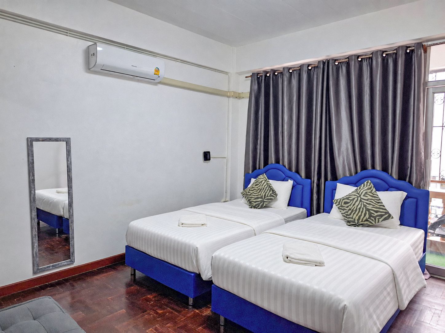 Habitación de hotel con dos camas, un espejo, un equipo de aire acondicionado y una ventana con cortinas.