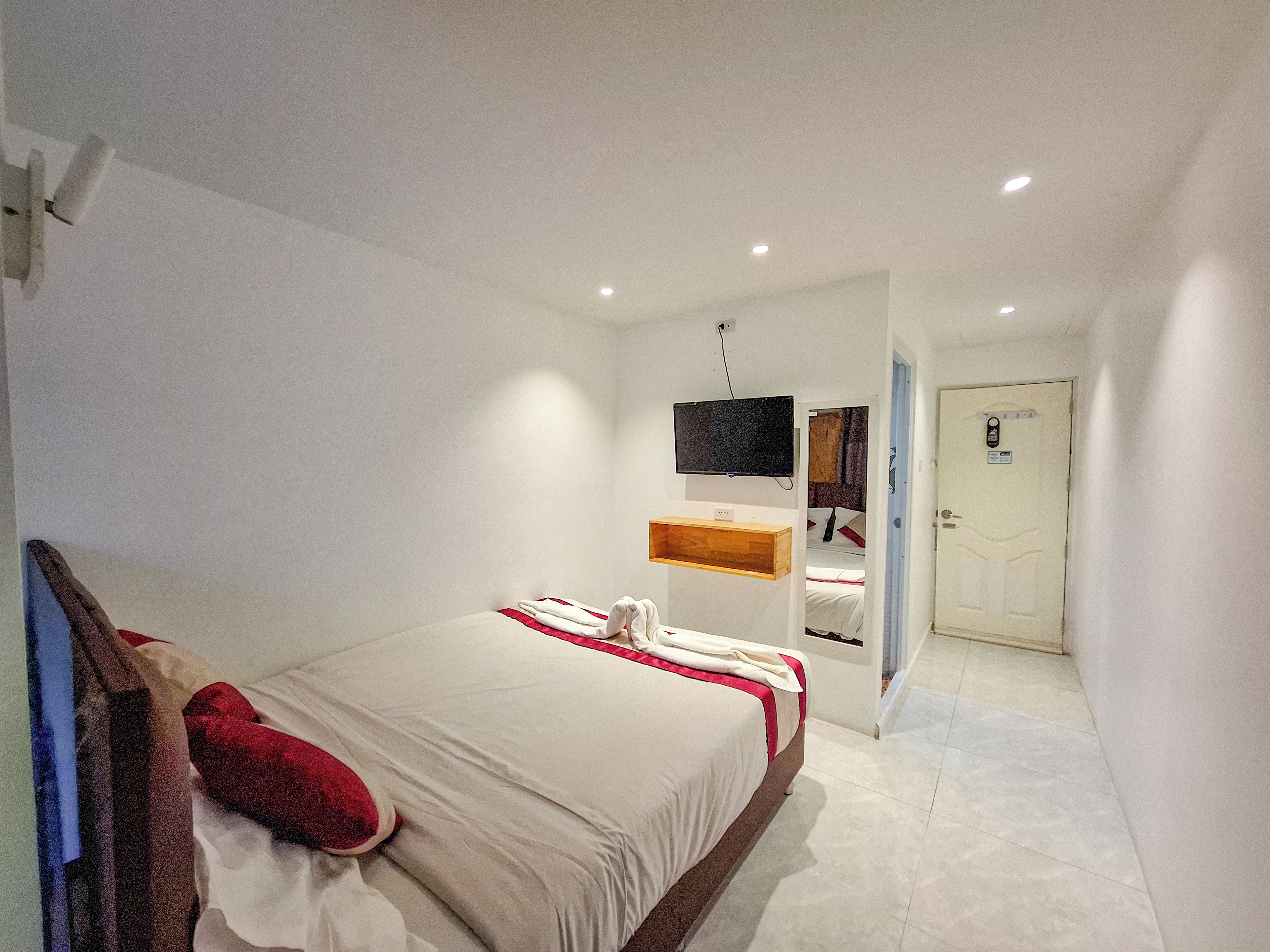 Ein Hotelzimmer mit einem Bett, einem an der Wand montierten Fernseher und einer Tür zu einem weiteren Raum.