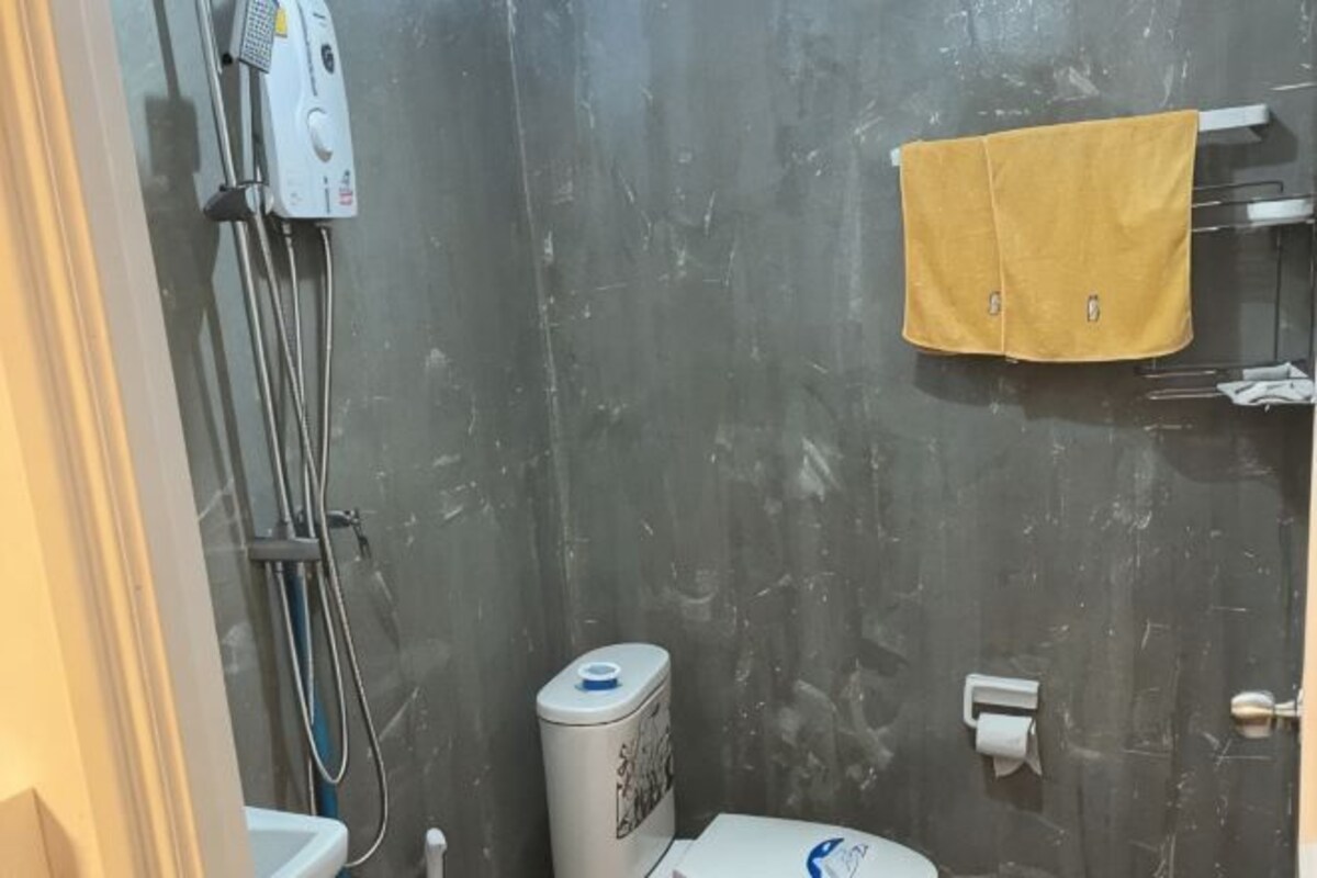 Une salle de bain équipée d’une douche, de toilettes, d’un porte-serviettes avec une serviette jaune et d’un chauffe-eau.