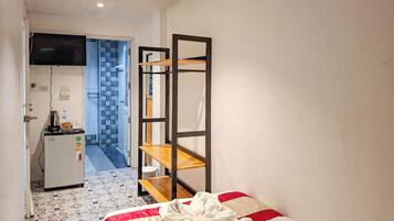 Ett kompakt hotellrum med en säng, ett litet kök och ett badrum som syns genom en öppen dörr.