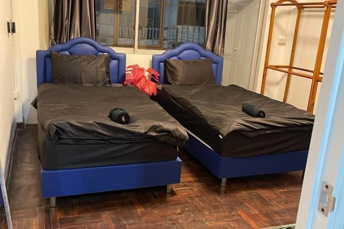 A room with two beds, each with a blue headboard and black bedding.
