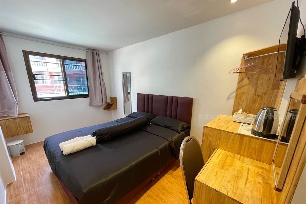 A modern hotel room with a single bed, a wooden desk, a chair, a television, and a window with curtains.