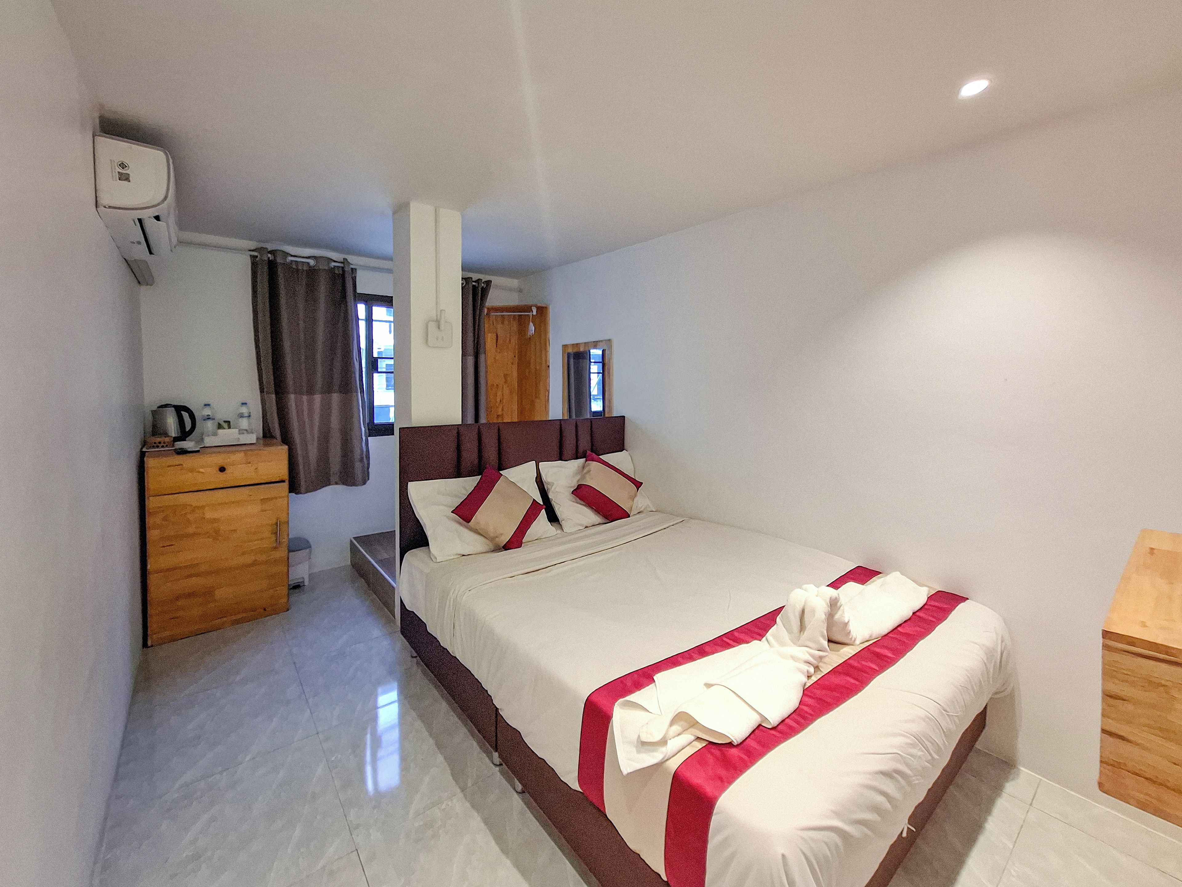 Une chambre d’hôtel avec un lit, une commode en bois, un miroir et une fenêtre avec des rideaux.