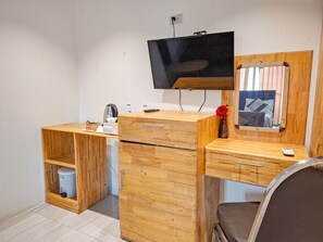 Habitación compacta con un escritorio de madera, un televisor fijado a la pared, un espejo y una silla accesible para sillas de ruedas.