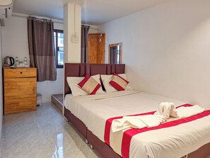 Een hotelkamer met een bed, een houten dressoir, een raam met gordijnen en een spiegel aan de muur.